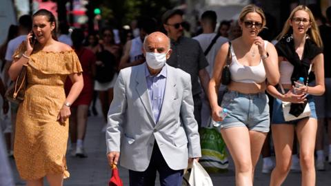 A shopper with a face mask on walks with other pedestrians on Oxford street in central London