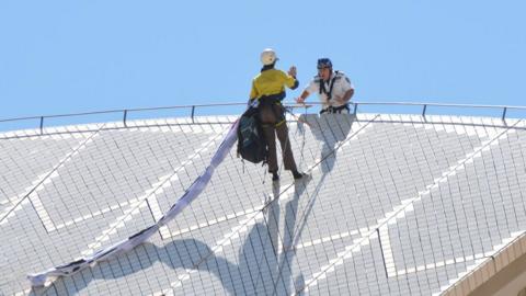 A protester on top of the Sydney Opera House sails is approached by a policeman