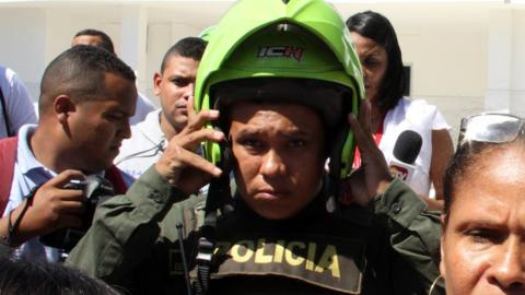 A police officer adjusts his helmet outside the scene of the ombing, surrounded by civilians