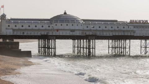 Brighton Pier from the side with waves crashing against the sand
