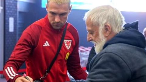 Aaron Ramsey signs an autograph for a fan at Cardiff Airport