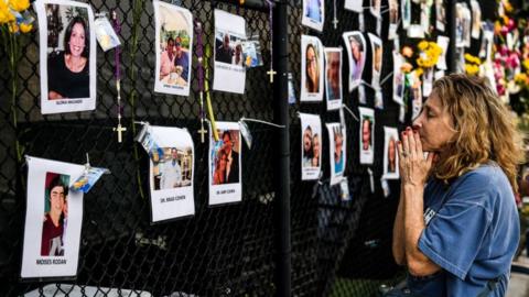 A woman prays in front of photos at the makeshift memorial for the victims of the building collapse, near the site of the accident in Surfside, Florida, north of Miami Beach on June 27, 2021
