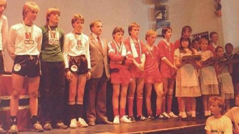 The Orkney U16s football team standing on stage with their bronze medals in 1985, the first year of the Island Games.