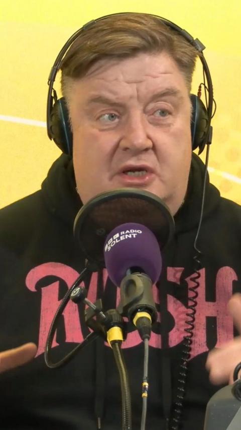 Adam Blackmore speaks into a purple microphone and wears headphones. 