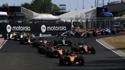 The McLaren of Lando Norris is pushed into position by his mechanics on the grid before the start of the Hugarian Grand Prix