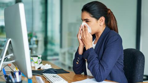 A woman at a desk blowing her nose