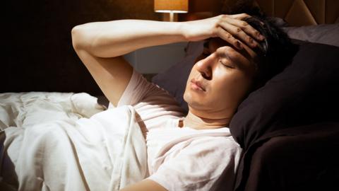 Asian man in bed suffering insomnia and headache, thinking about his problem at night - stock photo