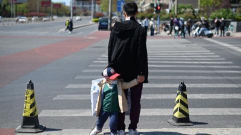 A man leading a face mask-clad child waits to cross a street in Beijing on April 11, 2020, amid the COVID-19 coronavirus pandemic