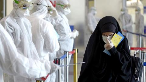 Medical staff in protective gear distribute leaflets to Iraqi passengers returning from Iran, 5 March 2020