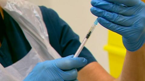 Nurse with gloved hands holds vaccine needle