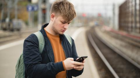 Young man looking at phone on train platform