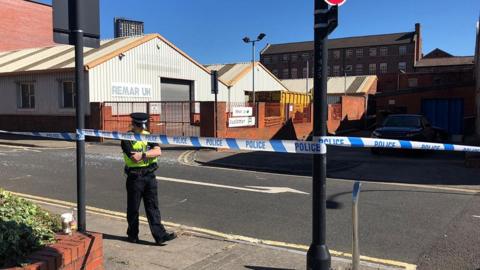 A police officer standing beside a road closed by police cordon tape