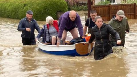 Handout photo of Simon O'Brien (left) using his homemade boat, which he built for his grandchildren, to rescue elderly residents from their home in the village of Debenham, Suffolk