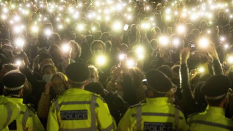 People at Saturday's vigil hold up torches and mobile phones in front of a line of uniformed police officers