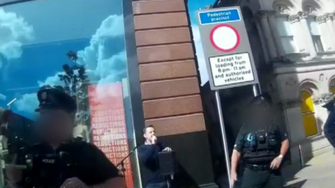 Footage showing two police officers standing near a man with a microphone and a public address system