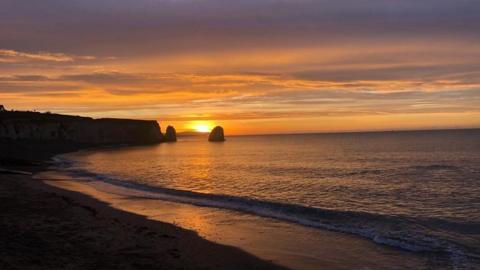 The sun rises over the sea with the headland to the left