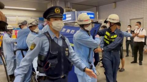 Police escort rescue workers carrying a person through a train station after a knife attack on a train in Tokyo