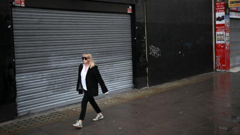 A pedestrian walks past the shuttered entrance to a closed-down store on Oxford Street in central London