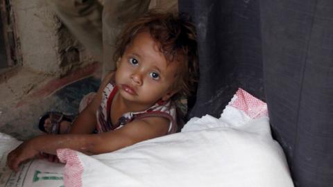 A Yemeni young child sits next to food rations that a local charity is distributed during Ramadan in 2016.