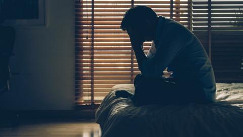 Man with head in hands sitting on a bed