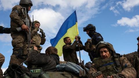 Ukrainian soldiers adjust a national flag atop a personnel armoured carrier on a road near Lyman, Donetsk, in October 2022