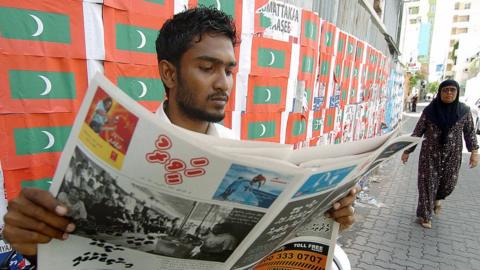 A Maldivian man reads a newspaper while sitting on a pavement in Mali