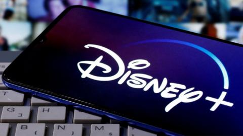 A smartphone with displayed Disney+ logo is seen on the keyboard