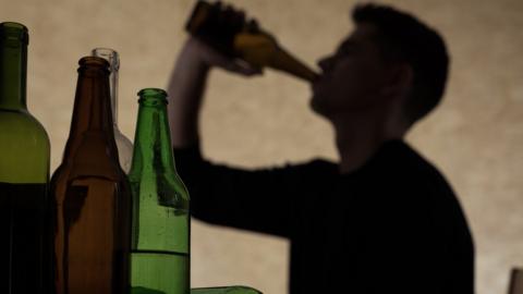 Silhouette of a man drinking a bottle of beer - lots of empty bottles are in the foreground