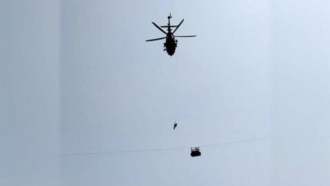 Army soldier slings down from a helicopter towards the cable