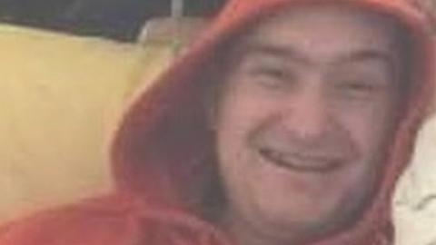 A slightly blurry photograph of Kamil Leszczynski smiling and wearing a red hooded top