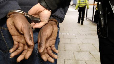 Stock image of a black person being handcuffed by a white police officer
