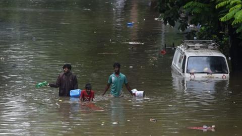 People wade through flood water in Mumbai. A partially submerged van is to the right.