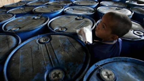 A child refugee from Myanmar plays among oil containers