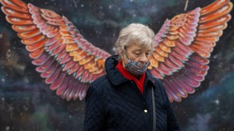 A woman wearing a faced mask in front of street art of angel wings