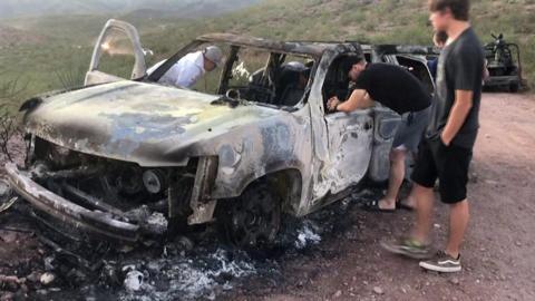 Relatives of the victims look over a burned-out car
