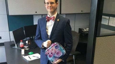 photo shows David Pendragon wearing a suit in an office and holding a lunchbox with pictures of cats on it.