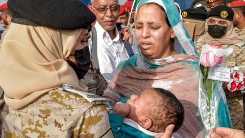 A Saudi Navy sailor assists a woman with a child who have been evacuated from Sudan after disembarking off a ferry passenger ship upon arrival at King Faisal navy base in Jeddah on April 26, 2023
