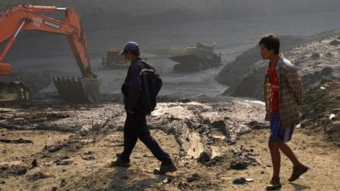 Two men walk past the 'mud lake' caused by the landslide in Kachin, with vehicles emerging from the mud