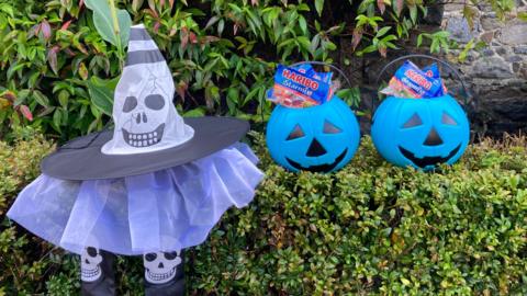 Blue Halloween buckets with sweets in on a hedge next to a Halloween decoration