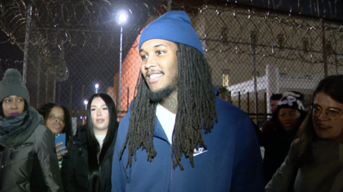 Darien Harris in blue hat and jacket in front of jail fence