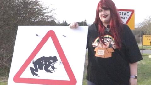 Hayley, aka 'Toad Girl', stood beside a toad crossing sign in Hexham