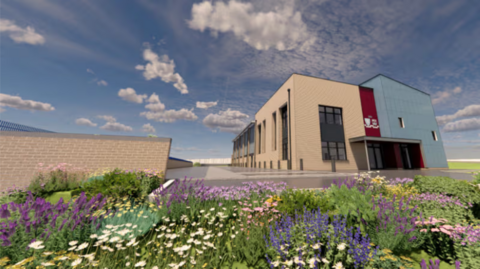 The image shows the outside of a school building, where plants and other flowers can also be seen. Clouds can be seen sparsely across the blue sky.