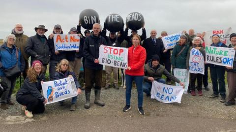 A group of people on a beach with banners opposing the use of biobeeds