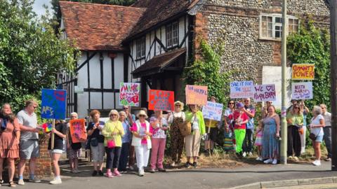 A group of campaigners standing in a line outside of Heath Barn holding signs and placards.
