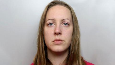 Lucy Letby police photograph - she is looking straight ahead. She has blond shoulder length hair, and is standing in front of a grey background 