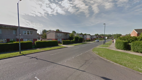 A road with houses on either side with a junction onto another road.