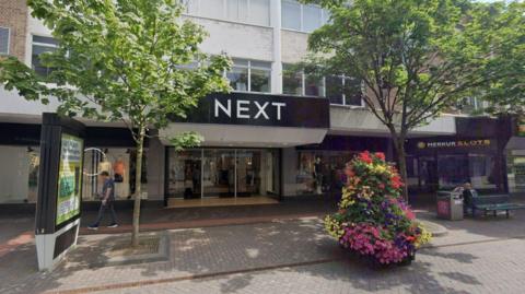 Next, on Middlesbrough's Linthorpe Road. A large sign with the firm's name is above the glass entrance doors. Flowers are planted in an area in front of the shop. There are also two small trees.