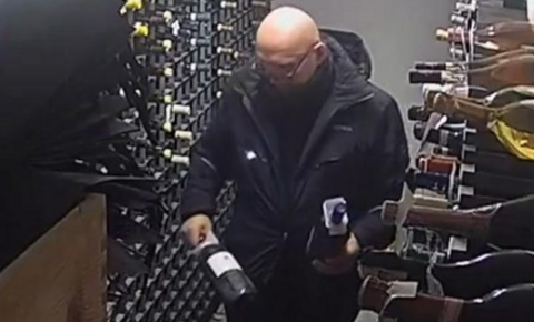 CCTV of an older man with a bald head in a wine cellar holding a bottle of wine