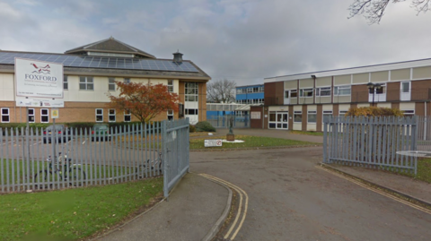 Street view of Foxford School & Community Arts College. The brick two-storey building is surrounded by a grey metal fence