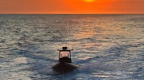 An RNLI rescue RIB in the ocean moving towards the camera with an orange reflection in the water behind it from the beaming, low sun.